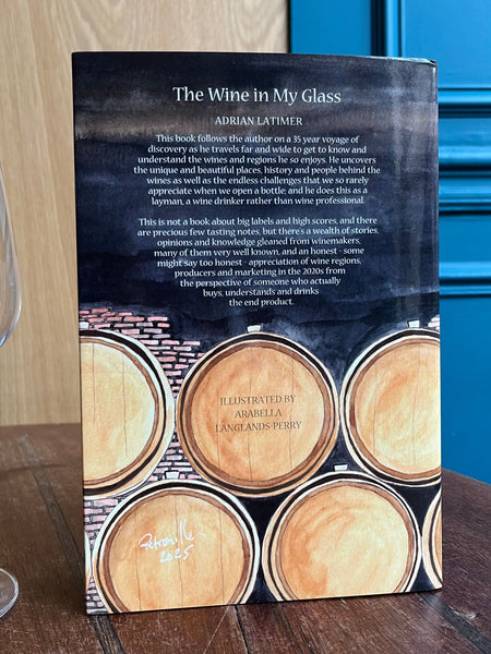 Book titled 'The Wine in My Glass' by Adrian Lattimer on a wooden surface with a glass of wine.
